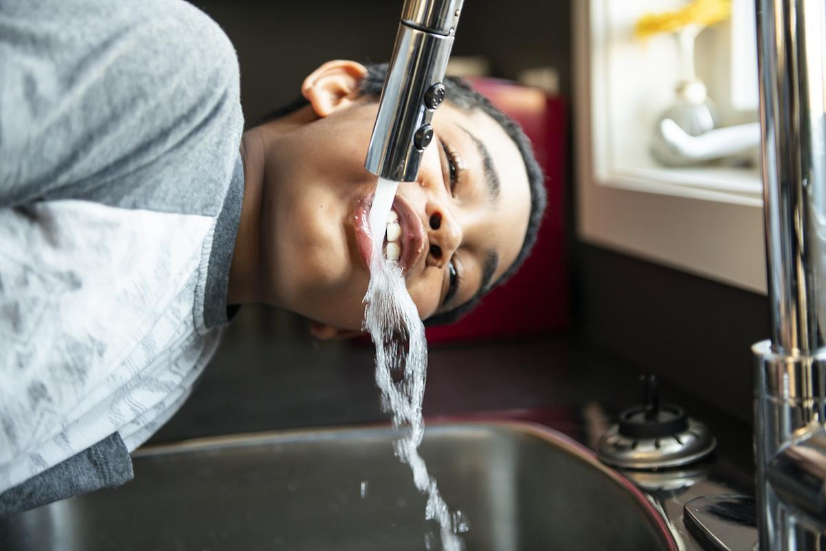 A child drinks from a water faucet or tap above a sink.