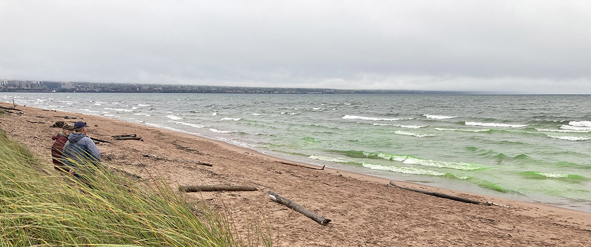 Duluth, Minnesota, Park Point Beach showing food-grade green dye in Lake Superior and two people standing on the beach.