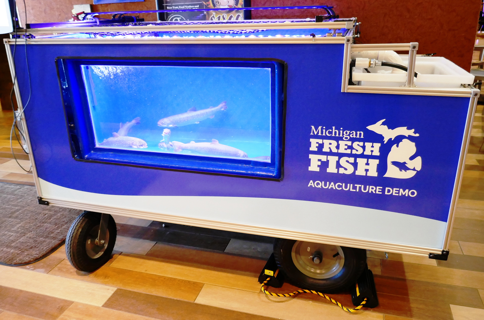 Fish tank on a wheeled cart. Sign reads: Michigan Fresh Fish aquaculture demo.
