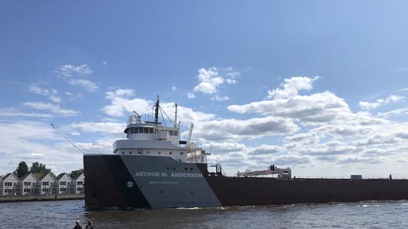 Two people on a jetski passing in front of a tanker ship on Lake Superior.