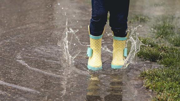 Person wearing rain boots and splashing in a puddle of water.