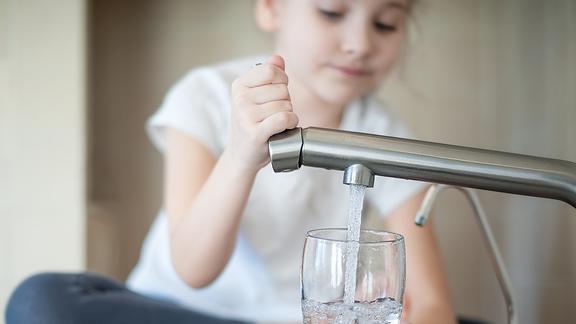 Young child sitting on counter filling glass from water faucet.
