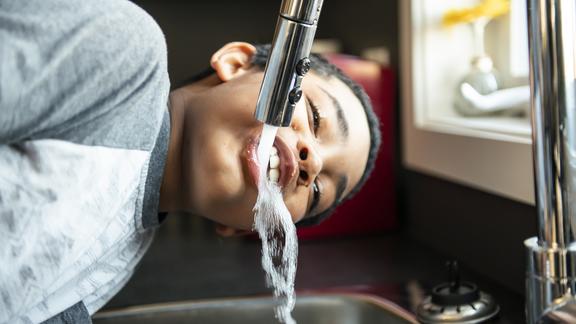 A child drinks from a water faucet or tap above a sink.