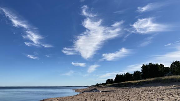 Sandy beach, lakeshore, pine trees, and blue sky with streaks of high clouds