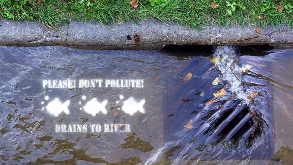 Image of stormwater running into a drain next to a stencil that says Please Don't pollute, drains to river.