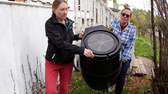 two people carry a rain barrel