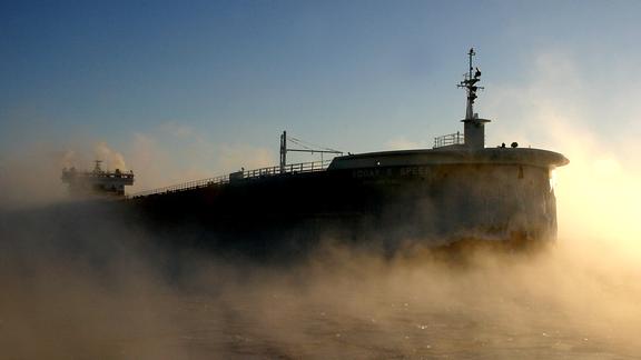 A Great Lakes freighter silhouetted against the sun and steam rising from the lake.