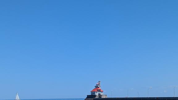 Clear blue skies and calm waters with a sailboat and lighthouse at the entrance of the Duluth port 