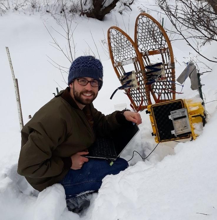 Person crouching in snow with snow shoes while checking scientific equipment.