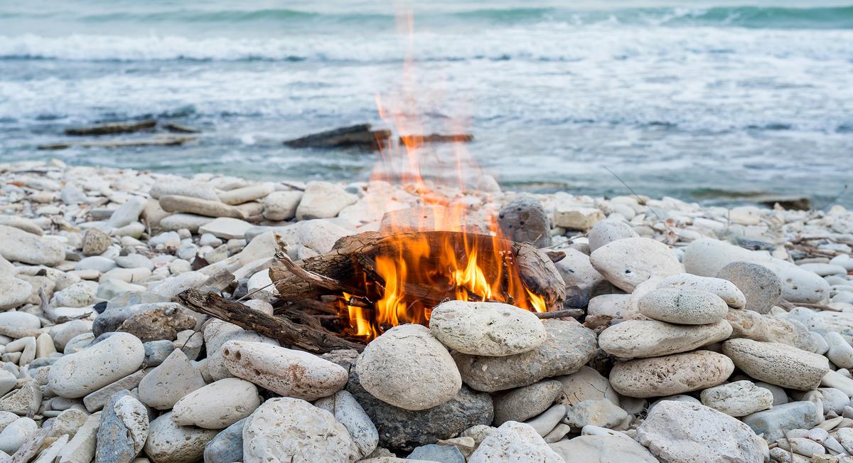 Beach bonfire on rocky shore by water with waves. 