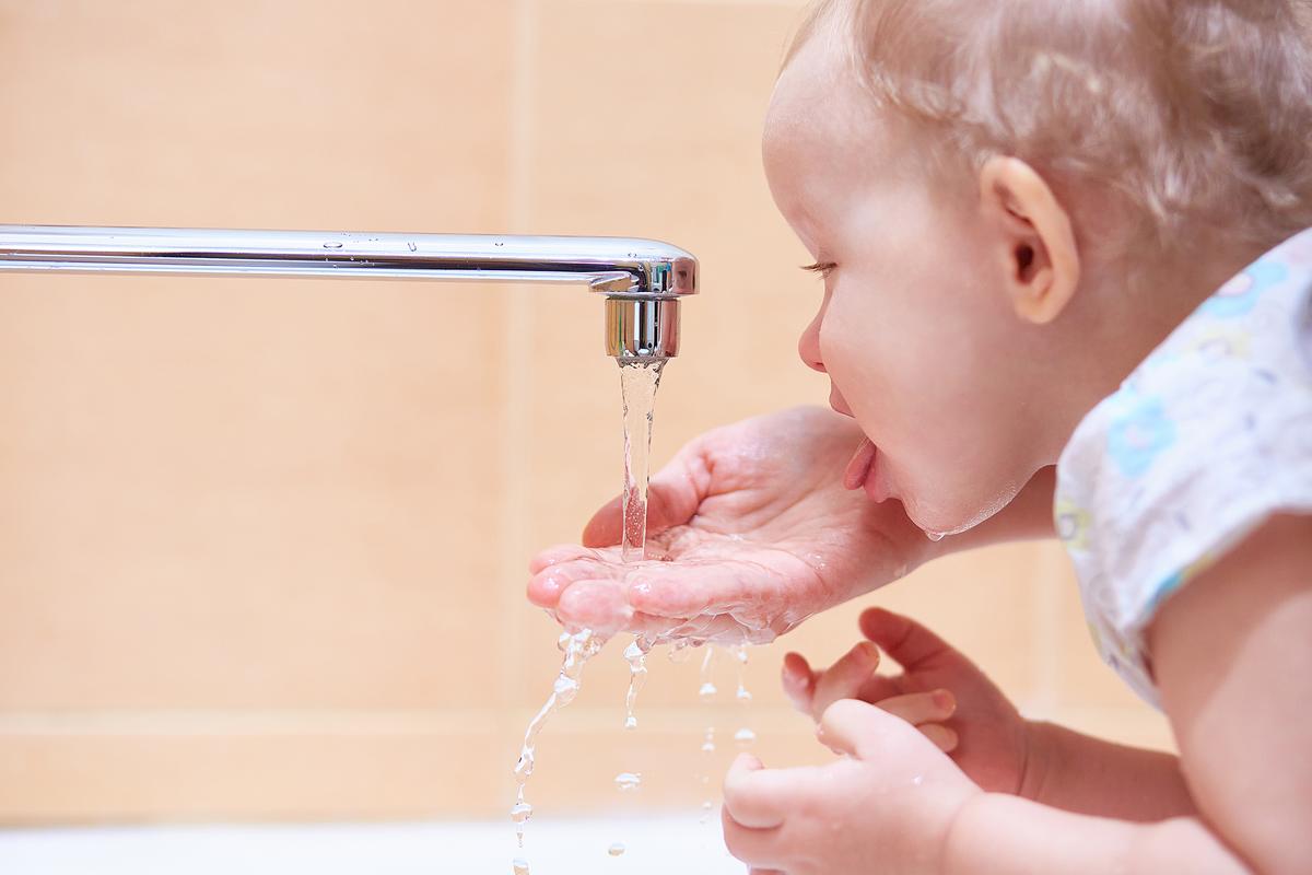 A small child is helped to drink running water from a faucet or tap. 