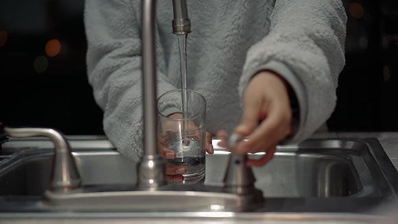 Person filling up glass with water from tap.