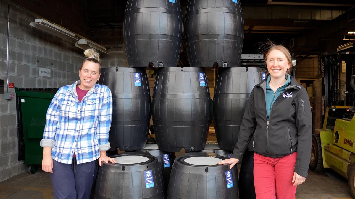 Tiffany Sprague from NRRI and Madison Rodman from MNSG stand in front of a tower of rain barrels