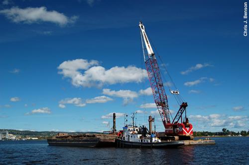 A boat next to a barge with a crane.