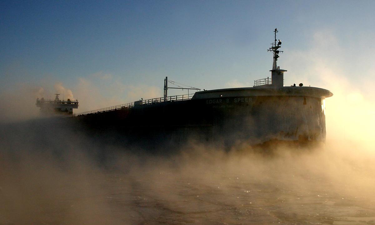 A Great Lakes freighter silhouetted against the sun and steam rising from the lake.