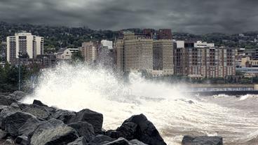 Waves crashing onto rocks in front of buildings